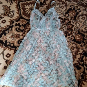 Ljusblå spetsklänning med blommigt mönster - Säljer en romantisk ljusblå klänning med tunna axelband och vacker spets med blommigt mönster. Klänningen är genomskinlig och har en lätt och luftig känsla, perfekt för varma dagar eller som ett statement-plagg.