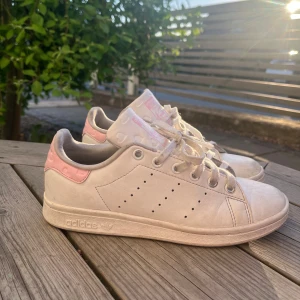 Adidas Stan Smith sneakers med rosa detaljer - Snygga Adidas Stan Smith sneakers storlek 36 2/3 men dem passar även om man har storlek 37. Vita med ljusrosa hjärtan på häl och plös. Säljer för dem inte passar långre. Dem är ganska använda men dem tvättas innan dem skickas. Köpt för 800kr men säljs för 400kr 