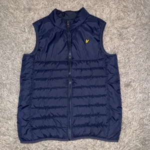 Blå dunväst från Lyle & Scott! - Mörkblå dunväst från Lyle & Scott med gul logotyp på bröstet. Ny skick använd 3 gånger 10/10 De är storlek 14/15 år, den sitter som S och M funkar också till XS! Nypris 800kr och jag säljer för endast 450krVästen har ståkrage, dragkedja framtill och quiltad design. Perfekt för lager-på-lager och enkel att matcha med olika outfits.