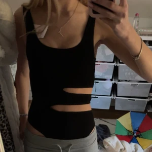 Svart body med cut-outs - Säljer en svart bodu med breda axelband och trendiga cut-outs vid midjan. Perfekt för dig som vill ha en stilren men edgy look. Toppen är figurnära och passar till många olika outfits. Den är ribbad