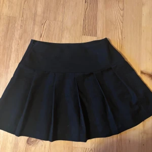 Svart kortkjol med utställd form - Enkel och stilren svart kortkjol från divided h&m med utställd passform. Kjolen har en tydlig midja och är sydd i ett mjukt material som ger ett snyggt fall. Perfekt att matcha med en crop top eller stickad tröja.