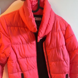 Rosa pufferjacka från H&M - Säljer en rosa pufferjacka från H&M med hög krage och dragkedja framtill. Jackan har lång ärm och två fickor med dragkedja. Perfekt för kyligare dagar och ger en färgklick till din outfit.