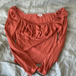 Rostfärgad ribbad topp från Bubbleroom - Trendig rostfärgad långärmad topp från Bubbleroom med ribbad struktur och rynkade detaljer vid bysten. Toppen har en bred, något fyrkantig ringning och är figurnära i modellen. Perfekt för att lyfta din vardagsstil.