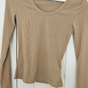 Beige ribbad långärmad topp - Säljer en beige långärmad topp med ribbad struktur och rund halsringning. Perfekt att styla till olika outfits och superenkel att matcha med andra plagg.
