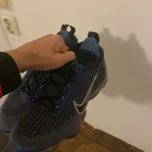 Blå Nike Air Vapormax sneakers - Säljer ett par blå Nike Air Vapormax sneakers med svart och vit swoosh. Skorna har snörning, mesh-överdel 