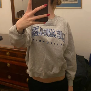 Grå sweatshirt med Los Angeles-tryck - Säljer en grå sweatshirt med blått Los Angeles-tryck på bröstet. Tröjan har rund halsringning och långa ärmar. Perfekt för en avslappnad stil❤️