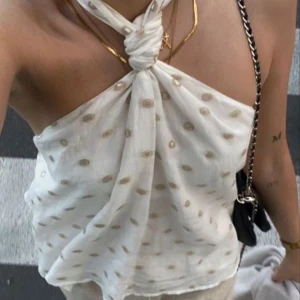 Vit halterneck topp med guldprickar - Säljer en snygg vit halterneck topp med knyt i nacken och små guldprickar. Tunt och luftigt material, perfekt för varma dagar. Styla med jeans eller kjol för en trendig look!
