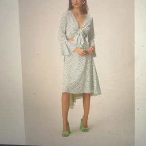 Ommlottklänning från ADOORE - Superfin ljusblå blommig omlottklänning med knyt framtill och v-ringning. Klänningen har långa volangärmar och är i ett lätt, luftigt material. Perfekt för vår och sommar! Aldrig använd.