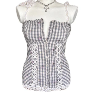 Guess korsett - Supersöt korsett-topp i gråvitt rutigt mönster med vita spetsband och snörningsdetaljer framtill. Toppen har smala axelband med spets och dekorativa knappar framtill. Finns en lös tråd på axelbandet som går att klippa bort 💓