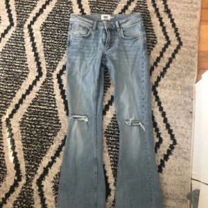 Ljusblå bootcut jeans med slitningar - Säljer ett par ljusblå jeans med bootcut passform och slitna detaljer vid knäna. Jeansen har klassiska fem fickor och normalhög midja. Perfekta för en avslappnad och trendig look.Aldrig använda!