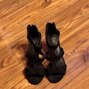 Svarta klackskor med dragkedja från Din Sko - Säljer ett par svarta klackskor från din sko med öppen tå och dragkedja baktill. Skorna har breda remmar och en stabil klack, perfekta för att lyfta din outfit.