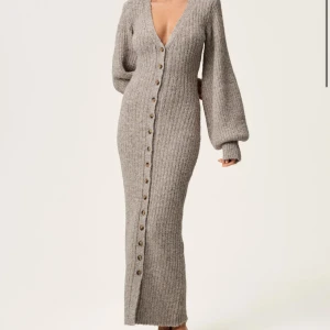 Stickad adoore klänning - Mysig beige stickad långklänning med v-ringning och långa puffärmar. Klänningen har knappar hela vägen framtill och en ribbad struktur som ger en snygg passform. Använd 1 gång, alltså i nyskick!