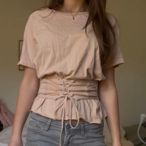 Beige topp med snörning från Bik Bok - Säljer en beige topp från Bik Bok i bomull med korta ärmar och snygg snörning i midjan. Säljs inte längre och är i storlek xs💞💞