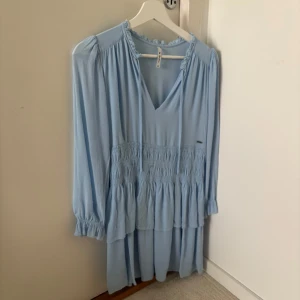 Ljusblå volangklänning  - ljusblå klänning med v-ringning, långa ärmar och volangdetaljer. 