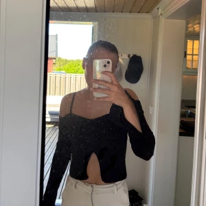 Svart offshoulder topp med lång ärm - Snygg svart offshoulder topp med lång ärm och croppad passform. Toppen har en unik skärning framtill och smala axelband. Perfekt för dig som vill ha en trendig och stilren look.