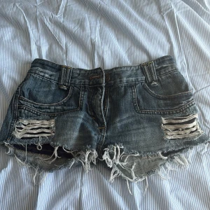Rippade jeansshorts från Tom Tailor - Säljer ett par blå jeansshorts från Tom Tailor med råa, fransiga kanter och slitna detaljer framtill. Klassisk femficksmodell med låg midja och bälteshällor. Perfekta för sommaren!