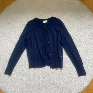 Mörkblå kofta från Holly & Whyte - Mörkblå kofta från Holly & Whyte by Lindex med rund halsringning och knappar framtill. Klassisk modell med långa ärmar och ribbade muddar. Har knappt används och är i fint skick. Originalpris 349 kr.