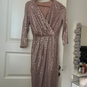 Glittrig långklänning med omlott och v-ringning - 💞OBS! Klänningen finns i både 36 och 38!!💞Säljer en glittrig långklänning i ljus champagnefärg med omlott och v-ringning. Klänningen har trekvartsärm och markerad midja. Perfekt för festliga tillfällen såsom bal! 