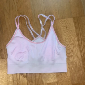 Ljusrosa sport-bh med korsade axelband - Säljer en ljusrosa sport-bh med tunna, korsade axelband och rosa kantband. Perfekt för träning och har en mjuk, stretchig passform. Enkel och stilren design. Från Röhnisch. 