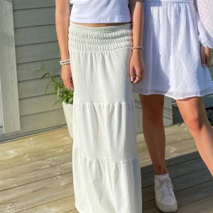 Vit långkjol med smock i midjan - Säljer en vit långkjol med bred smock i midjan och volangdetaljer. Kjolen har en luftig och flowy känsla, perfekt för varma dagar. Enkel att matcha med olika toppar för en fräsch look. Jag är 164 och säljer pga att den är lite kort💞💞💞🫰🏼