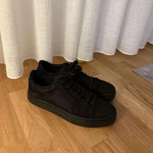 Svarta sneakers med snörning - Säljer ett par helsvarta sneakers med snörning och platt sula. Skorna har en stilren och enkel design som passar till det mesta. Perfekta för dig som gillar en clean och minimalistisk look.
