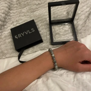 Grått pärlarmband från RYVLS - Säljer ett snyggt armband från RYVLS med gråmelerade pärlor och en metallisk detalj. Armbandet levereras i en elegant svart ask med genomskinligt lock. Perfekt accessoar för att lyfta din stil.