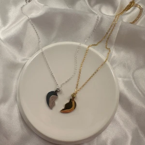 Halsband med hjärthänge i guld och silver - Två halsband med kedjor i guld- och silverfärg, båda med varsin halva av ett hjärta som hänge. Perfekt som vänskapshalsband eller för att dela med någon speciell. Hjärtana passar ihop som ett pussel.