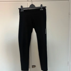 Svarta träningstights från SOC - Svarta tights från SOC med logga på benet. De är tighta och gjorda i ett stretchigt syntetmaterial, perfekta för träning eller gym. Klassisk modell med hög midja och smal passform.