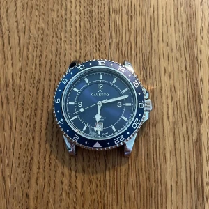Cavetto armbandsur med blå urtavla - Stilren klocka från Cavetto med blå urtavla, datumvisning och silverfärgad länk i metall. Klockan har en vridbar bezel med 24-timmarsmarkeringar och tydliga siffror. Levereras i svart box. Perfekt accessoar för dig som gillar klassisk design. Den har små reporn på länkarna och en minimal spricka på klockuret men syns inte om man inte kollar nära. Storleken är Diameter 42 mm, bredd 22 mm och längd på klockarbandet 21 cm länkarna på sista bilden går att sätta fast så att klockarmbandet blir längre
