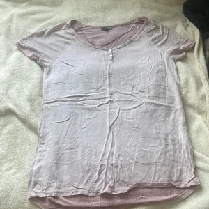 Ljusrosa t-shirt från Street One - Säljer en ljusrosa t-shirt från Street One med v-ringning och små knappar vid halsen. T-shirten har korta ärmar och är tillverkad i ett mjukt bomullsmaterial. Perfekt för vår och sommar!