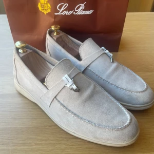 Beige Summer Walks Loro Piana - Säljer ett par beige loafers från Loro Piana, modellen Summer Walk. Skorna är i mjuk mocka med vit platt sula och har en klassisk, minimalistisk design utan snörning. Perfekta till sommar. Är en tight 44 men 43 går perfekt.