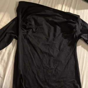 Svart offshoulder tröja - Snygg svart offshoulder tröja med långa ärmar. Perfekt för en elegant look. Materialet ser ut att vara mjukt och stretchigt, vilket ger en bekväm passform. Tröjan har en stilren design utan mönster eller extra detaljer.