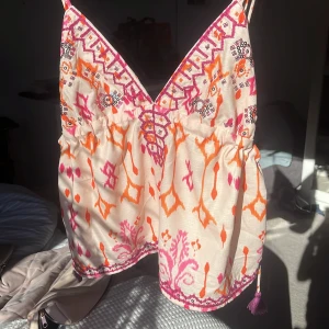 Mönstrad linnetopp från Design By Amor - Säljer en superfin linnetopp från Design By Amor i storlek XS. Toppen har smala axelband, v-ringning och ett färgglatt mönster i rosa, orange och vitt. Dragsko med tofs i sidan och broderade detaljer längs kanterna. HELT NY OCH OANVÄND!!🧡🤍🩷