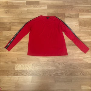 Röd långärmad tröja med ränder från Amisu - Röd långärmad tröja från Amisu med svarta och vita ränder längs ärmarna. Tröjan har en klassisk rund halsringning och är tillverkad i ett mjukt material som passar perfekt till vardags.