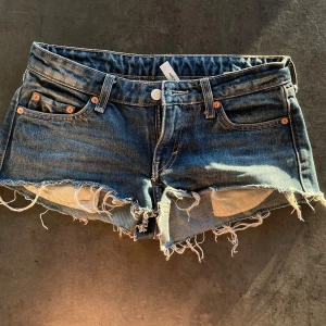 Blå jeansshorts från Weekday - Säljer ett par blå jeansshorts från Weekday. Shortsen har låg midja och är perfekta för varma dagar. Snygg och avslappnad stil med slitna detaljer.