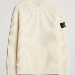 Stone Island, Vit stickad tröja  - Redan prutat och klart! Säljer en vit stickad tröja från Stone Island med klassisk patch på ärmen. Tröjan har ett grovt rutmönster och rund halsringning. Perfekt för dig som gillar stilrena och exklusiva plagg.