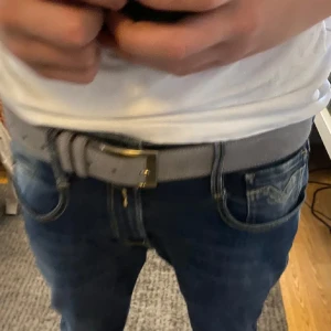 Grått mockabälte med silverfärgat spänne - Säljer ett stilrent grått bälte i mocka med ett klassiskt silverfärgat spänne. Perfekt accessoar för att lyfta din outfit. Bältet har en enkel design och passar till jeans eller chinos.