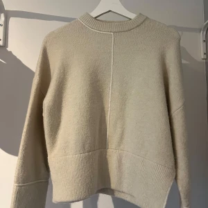 Beige stickad tröja från ZARA - Säljer en beige stickad tröja från ZARA i storlek XS. Tröjan har lång ärm, ribbade muddar och nederkant samt en dekorativ söm framtill. Aldrig använd, endast testad.