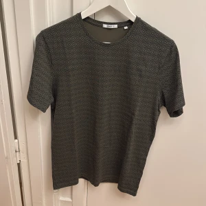 Mönstrad t-shirt från Bläck - Säljer en khakifärgad t-shirt från Bläck med diskret geometriskt mönster. T-shirten har rund halsringning och korta ärmar. Perfekt för dig som gillar stilrena men ändå unika plagg.