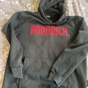 Svart och grå HOODRICH hoodie - Två hoodies från HOODRICH i storlek medium. En svart med röd logga och en grå med blå logga. Båda har huva, magficka och ribbade muddar. Perfekt för en avslappnad streetwear-look.