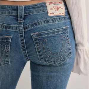 Blå bootcut jeans från True Religion - Säljer ett par klassiska blå jeans från True Religion med bootcut-passform och låg midja. Jeansen har tydliga sömmar och ikoniska bakfickor med broderad logga. Använt fåtal gånger💞