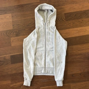 Ljusgrå zip-hoodie med huva från Peak Performance - Ljusgrå zip-hoodie med huva från Peak Performance.  zip-hoodien har två fickor framtill och justerbar dragsko i huvan. Tillverkad i mjuk bomullsblandning, perfekt för en sen sommarkväll.