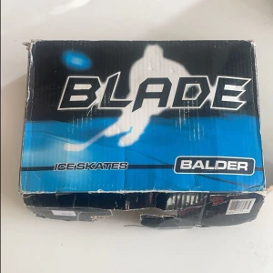 Svarta och vita skridskor från Blade Balder - Säljer ett par svarta och vita skridskor från Blade Balder. Klassisk design med vita snören och detaljer, samt robust svart syntetmaterial. Perfekta för isaktiviteter och levereras med skydd till skorna. Helt nya.