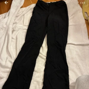 Svarta bootcut kostymbyxor från BikBok - Svarta kostymbyxor från BikBok med bootcut-passform och hällor för bälte. Byxorna har diskreta bakfickor och stängs med dragkedja och knapp. Perfekta till en snygg och stilren look.