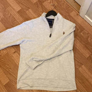 Ljusgrå halvzip tröja från U.S. Polo Assn. - Säljer en ljusgrå långärmad halvzip tröja från U.S. Polo Assn. Tröjan har en liten broderad logga på bröstet och hög krage med dragkedja. Perfekt för lager-på-lager och enkel att matcha med det mesta.