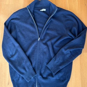 Mörkblå ziptröja i kashmir från Soft Goat - 100% Kashmirtröja från soft goat - använd men väldigt väl omhändertagen - lappen på insidan har lossnat i vänstra hörnet. Går väldigt enkelt att fixa ifall det önskas 