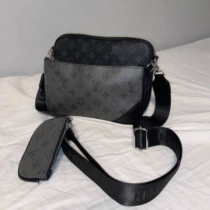 Svart trio axelväska set - Säljer en trio väska med klassiskt monogrammönster. Väskorna har silverfärgade detaljer och dragkedja, tillverkade i skinn. Perfekt för dig som vill ha en stilren och lyxig accessoar. Vid intresse skriv till mig privat😝