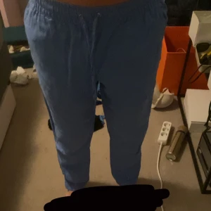 Blå linnebyxor  med snörning - Blå linnebyxor med resår i midjan och snörning framtill. Byxorna har en avslappnad passform. De är croppade vid anklarna och gjorda i mjukt bomullsmaterial.