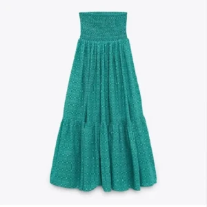 Turkos långkjol med mönster - Superfin turkos långkjol med geometriskt mönster och smock i midjan. Kjolen har volangdetaljer och är gjord i ett lätt och luftigt bomullstyg, perfekt för varma dagar. Sitter skönt och ger en avslappnad men ändå snygg look.