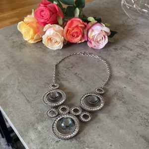 Statement halsband med silverfärgade cirklar - Unikt statement halsband i silverfärg med stora cirkulära hängen dekorerade med glittrande stenar och gråa facetterade detaljer. Kedjan är i metall och designen är riktigt iögonfallande och cool, perfekt för att lyfta vilken outfit som helst.